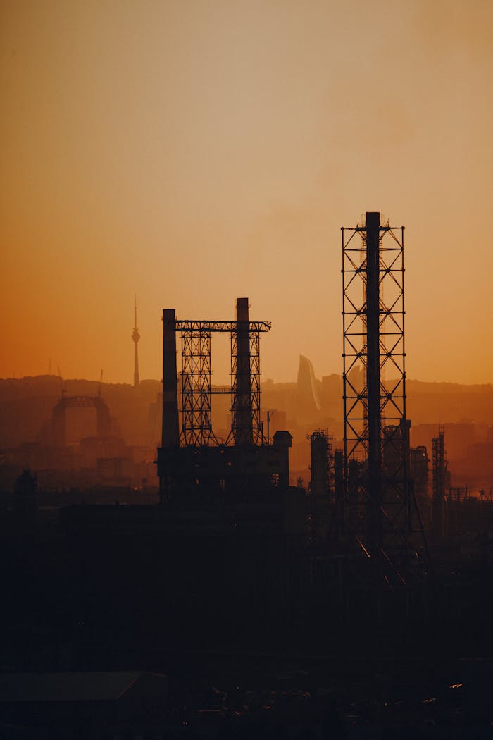 Dark silhouettes of urban industrial structures against a vibrant sunset sky.