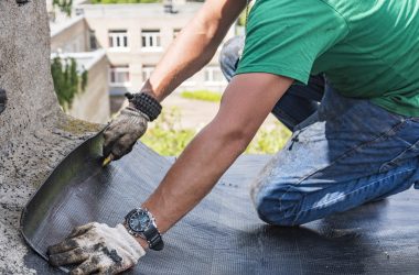 A construction worker cuts waterproofing material and prepares it for installation. Overhaul of the roof of the house.